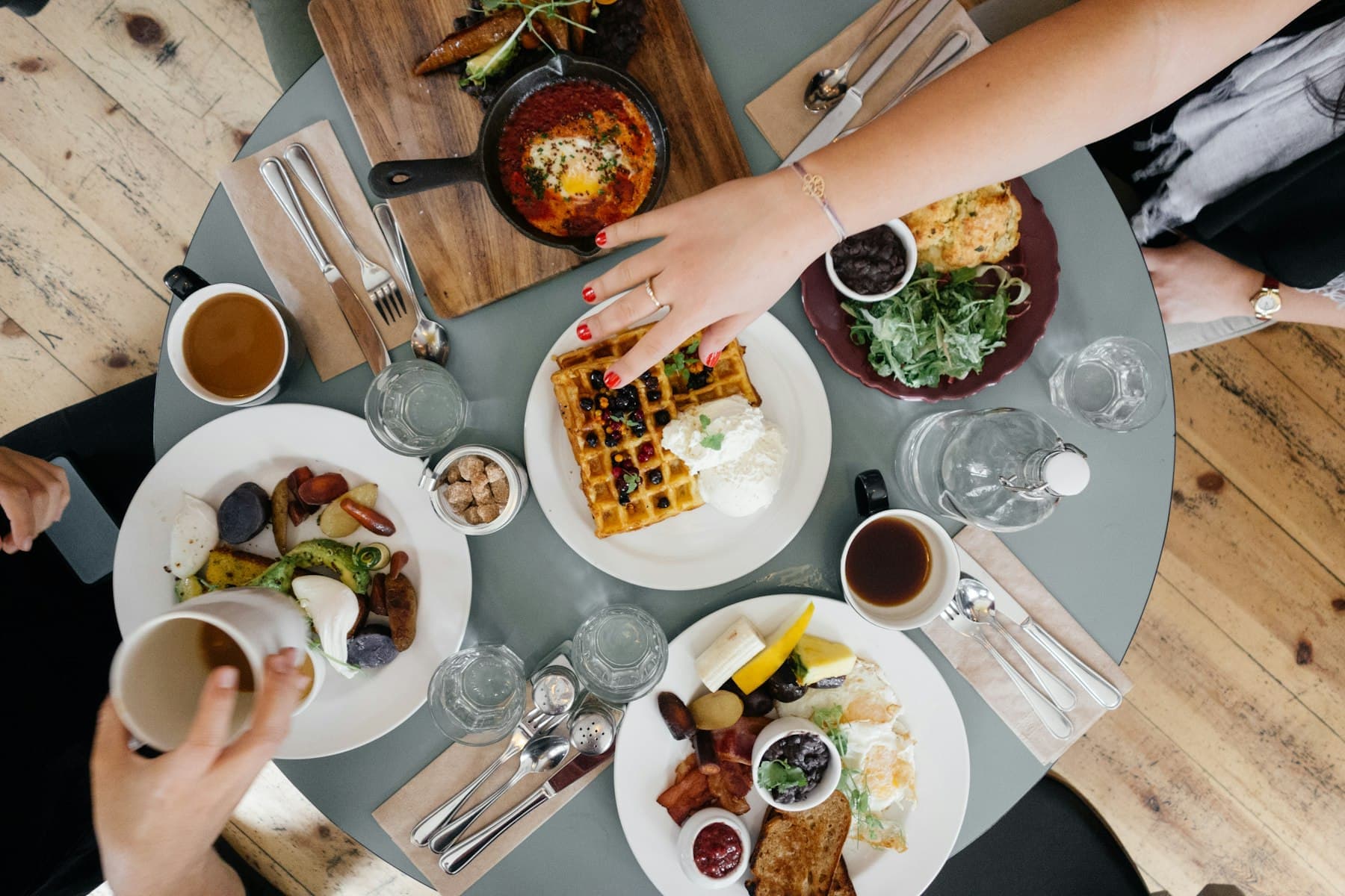 Friends reaching across a table of shared dishes