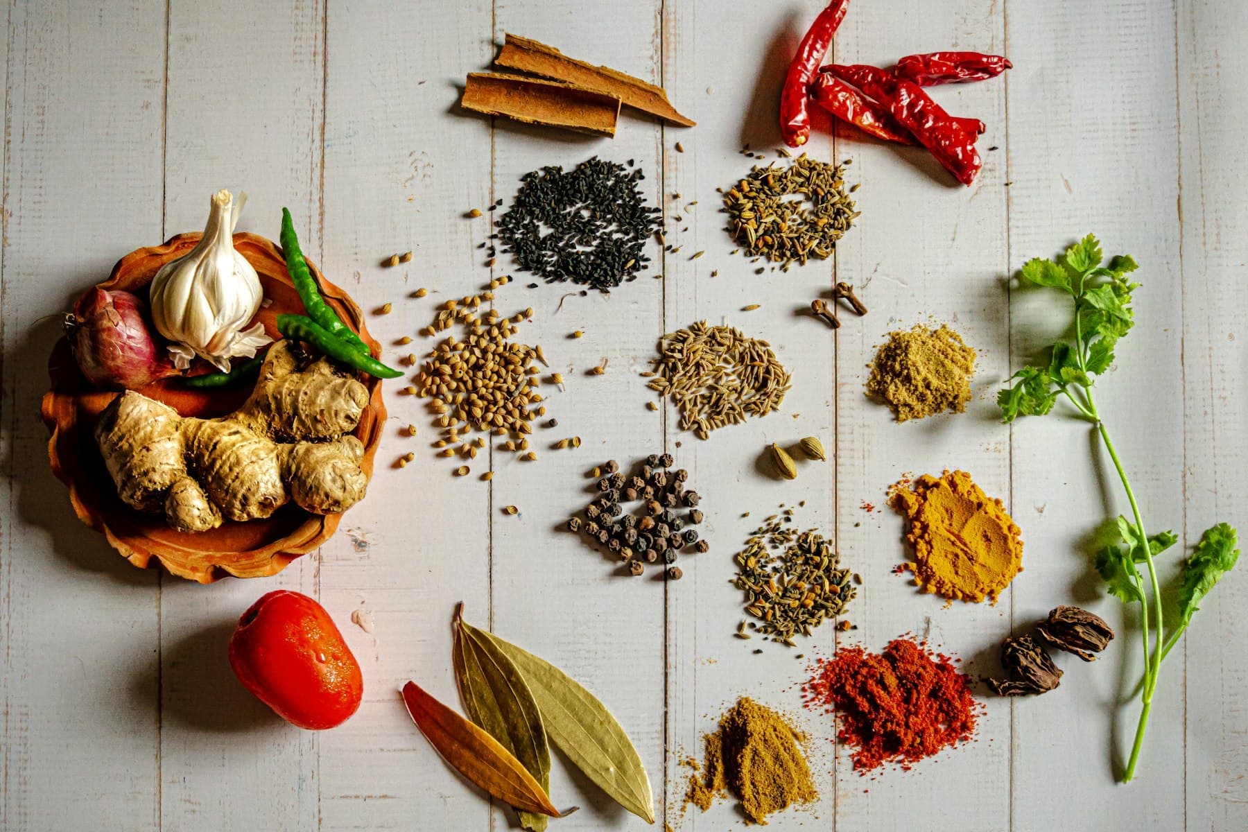 Whole and ground spices laid out on a white wooden table